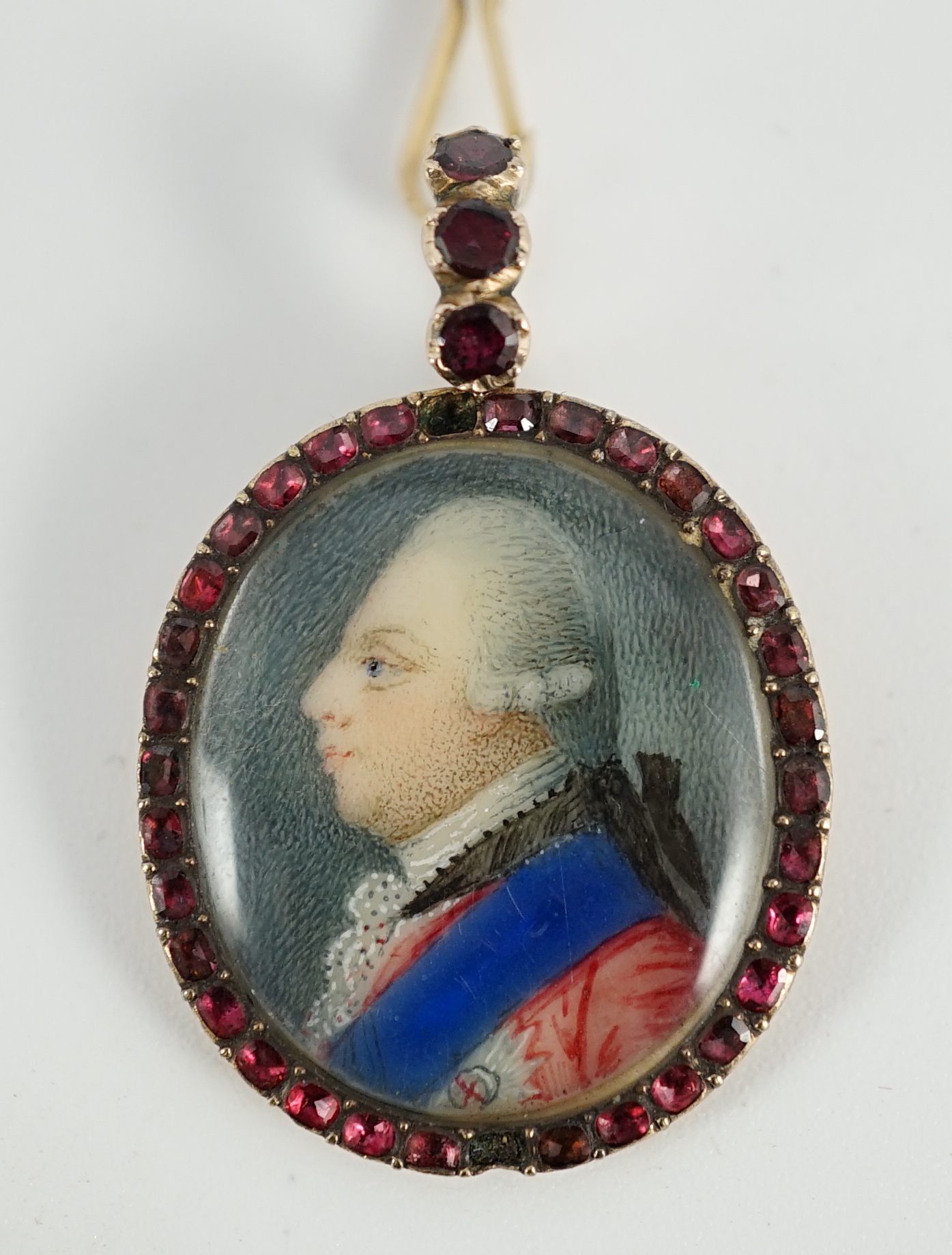 A George III Royal Presentation gold mounted and garnet set oval pendant, with inset miniature portrait of a gentleman to dexter, verso engraved 'The Gift of Queen Charlotte to E. Whitfield, 1770